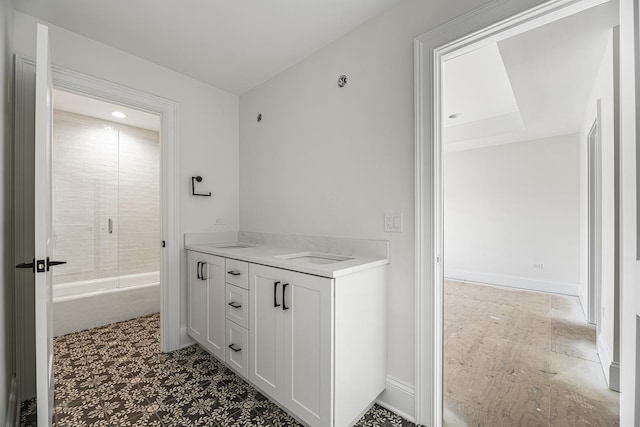 bathroom with a sink, a tile shower, double vanity, and baseboards