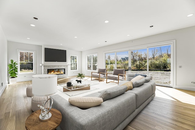 living area featuring baseboards, light wood finished floors, a glass covered fireplace, and recessed lighting