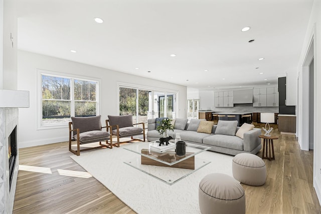 living area featuring light wood finished floors, a high end fireplace, baseboards, and recessed lighting