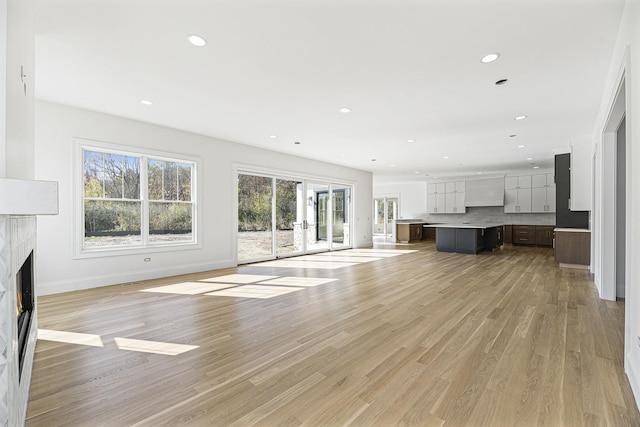 unfurnished living room with recessed lighting, a high end fireplace, light wood-style flooring, and baseboards