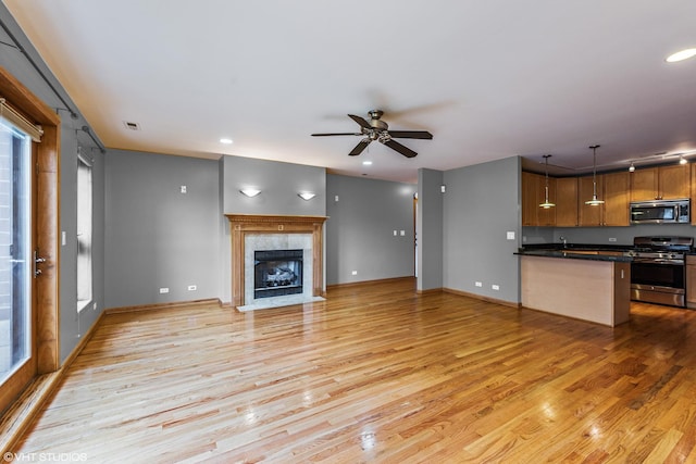 unfurnished living room with baseboards, light wood-type flooring, a fireplace, and a ceiling fan