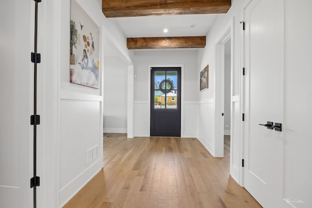 doorway featuring visible vents, wainscoting, beamed ceiling, baseboards, and light wood finished floors