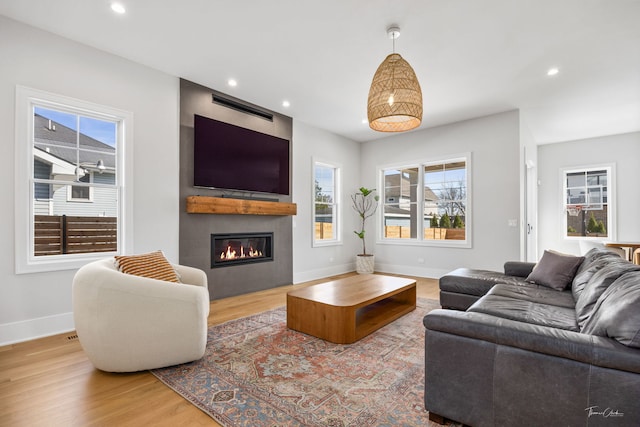 living room featuring a glass covered fireplace, baseboards, recessed lighting, and wood finished floors