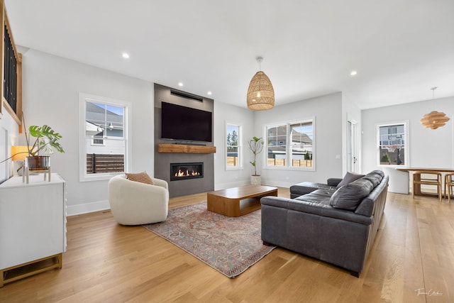 living room featuring recessed lighting, light wood-style flooring, a glass covered fireplace, and baseboards
