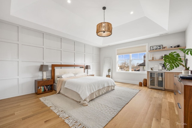 bedroom featuring light wood-type flooring, wine cooler, a decorative wall, and a tray ceiling