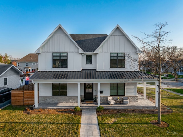 modern inspired farmhouse featuring a shingled roof, board and batten siding, a front yard, covered porch, and metal roof