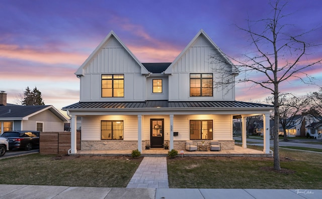 modern farmhouse with a front lawn, board and batten siding, covered porch, and stone siding