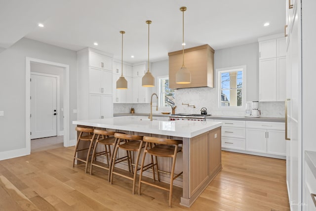 kitchen featuring light countertops, an island with sink, a sink, and tasteful backsplash