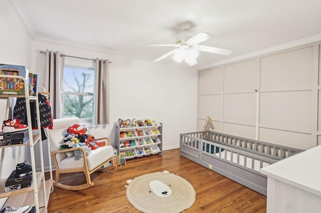 bedroom featuring a nursery area, ceiling fan, ornamental molding, and wood finished floors