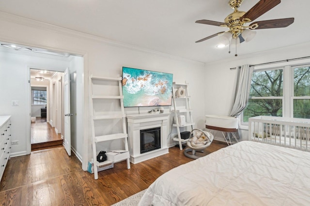 bedroom featuring a glass covered fireplace, baseboards, ornamental molding, and wood finished floors