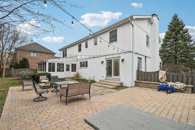rear view of property with fence, board and batten siding, a sunroom, and a patio area