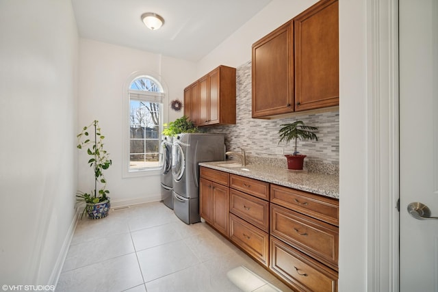 laundry area featuring baseboards, a sink, cabinet space, washing machine and dryer, and light tile patterned flooring
