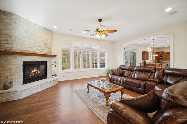 living area featuring a fireplace, arched walkways, a ceiling fan, wood finished floors, and baseboards