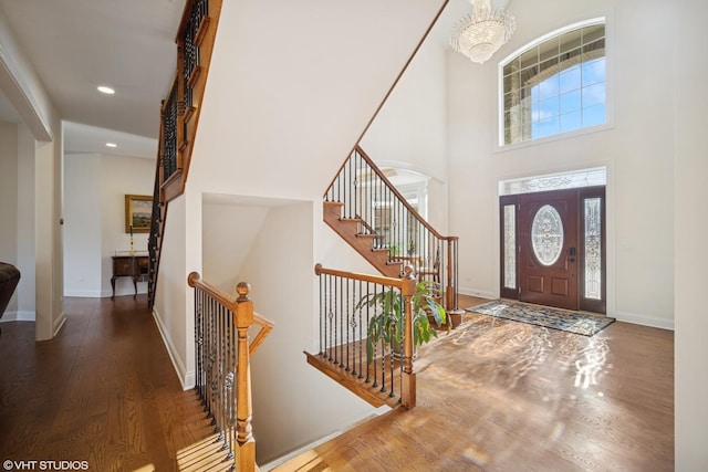 foyer featuring baseboards, a chandelier, wood finished floors, and a high ceiling