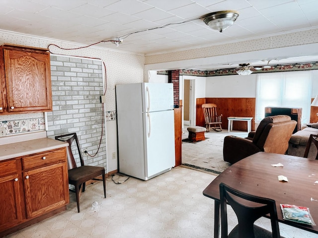 kitchen with brown cabinets, wallpapered walls, freestanding refrigerator, and light floors
