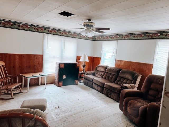 living room featuring wood walls, a wainscoted wall, wood-type flooring, and ceiling fan