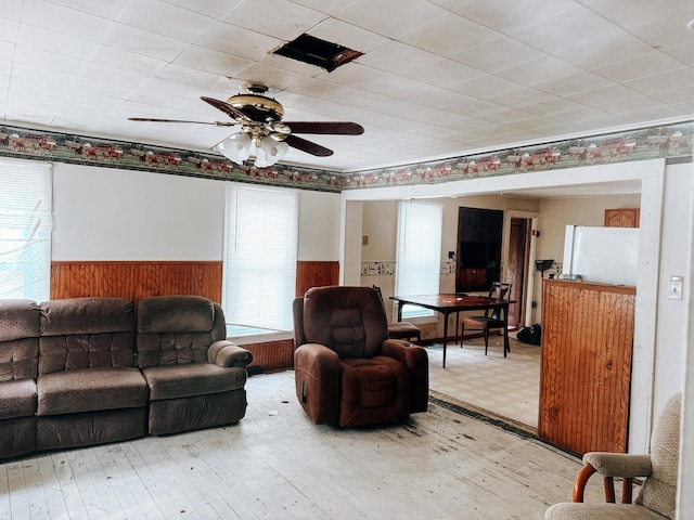 living area with wood walls, a ceiling fan, and a wainscoted wall