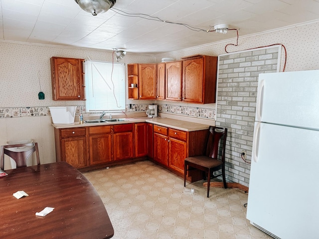 kitchen featuring freestanding refrigerator, light floors, ornamental molding, a sink, and wallpapered walls