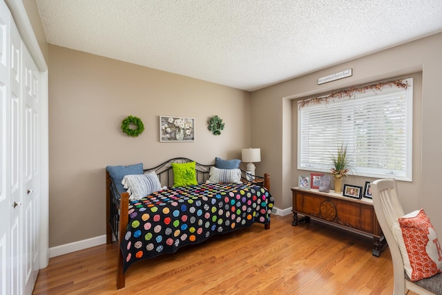 bedroom featuring light wood-type flooring, a closet, baseboards, and a textured ceiling
