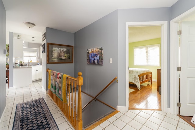 hallway featuring an upstairs landing, light tile patterned floors, and baseboards