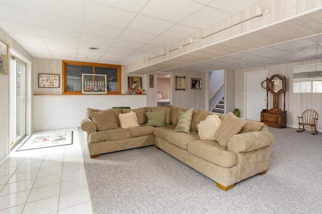 carpeted living room featuring stairs, a drop ceiling, tile patterned flooring, and wood walls