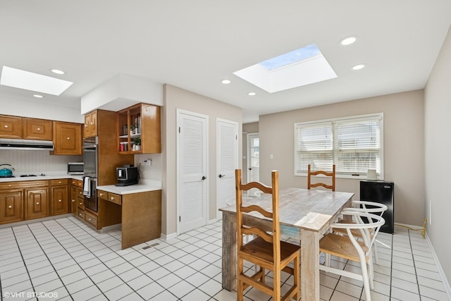 1130 Crestwood Dr, Northbrook, IL 60062 - kitchen featuring under cabinet range hood, brown cabinets, decorative backsplash, and a skylight