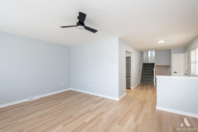 unfurnished living room with light wood-type flooring, baseboards, stairway, a ceiling fan, and visible vents