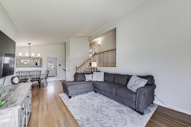 living area with a chandelier, wood finished floors, baseboards, and stairway