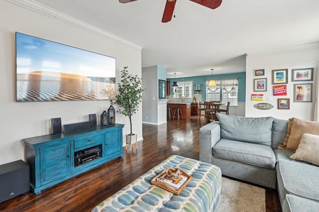 living area featuring dark wood-type flooring, ornamental molding, baseboards, and a ceiling fan