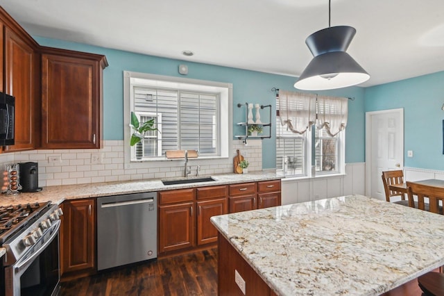 kitchen featuring dark wood-style flooring, light stone counters, wainscoting, appliances with stainless steel finishes, and a sink