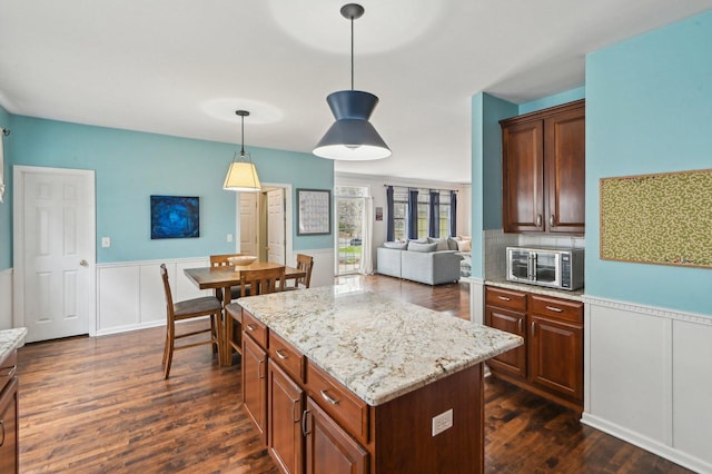 kitchen featuring hanging light fixtures, dark wood-style floors, a center island, and wainscoting