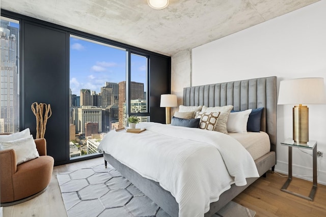 bedroom featuring baseboards, wood finished floors, access to outside, a view of city, and floor to ceiling windows