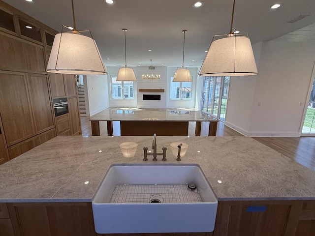 kitchen with baseboards, a fireplace, open floor plan, a center island with sink, and a sink