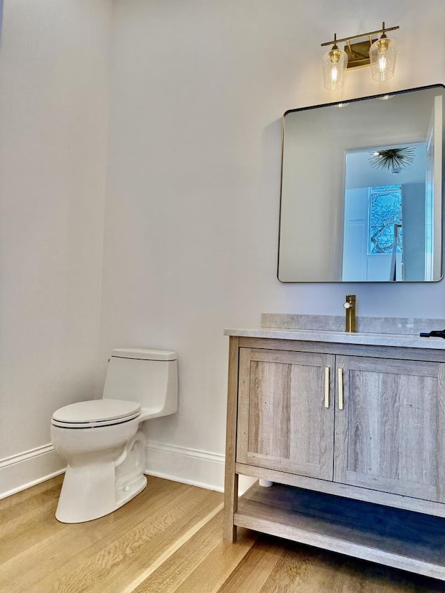 half bathroom with vanity, baseboards, toilet, and wood finished floors