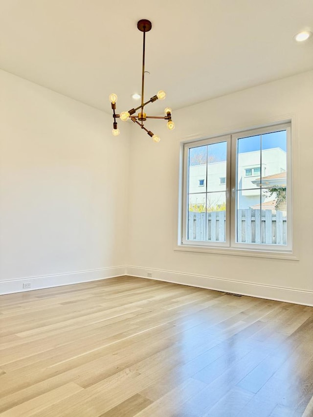 spare room featuring light wood-type flooring, an inviting chandelier, baseboards, and recessed lighting