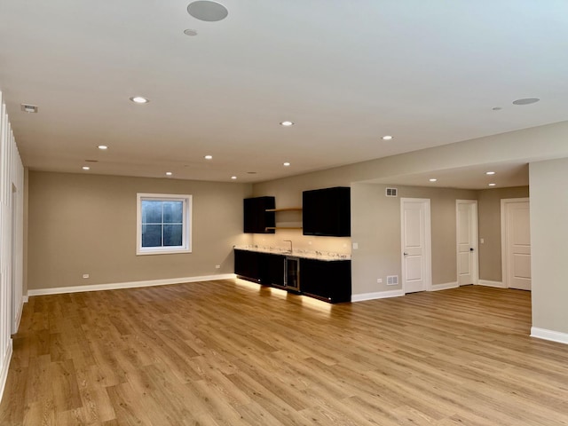 unfurnished living room featuring light wood-style floors, indoor wet bar, visible vents, recessed lighting, and baseboards