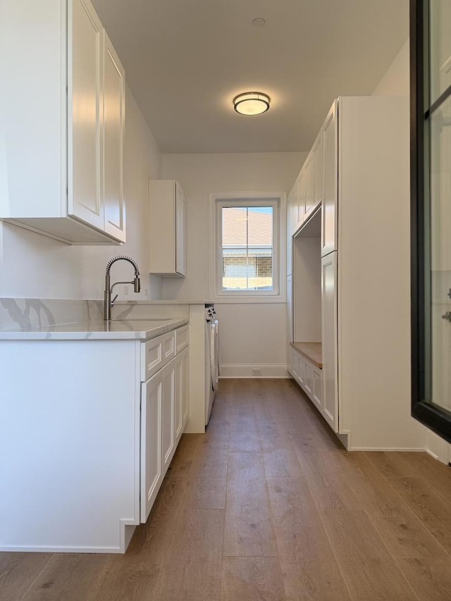 kitchen with white cabinets, light wood-type flooring, and a sink