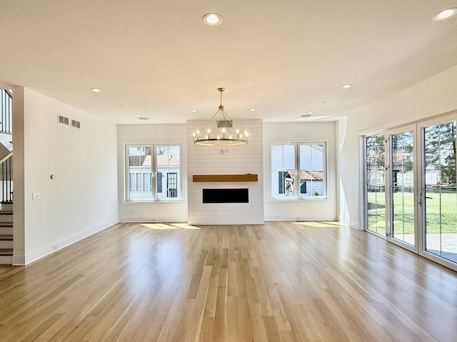 unfurnished living room with a healthy amount of sunlight, an inviting chandelier, visible vents, and stairs