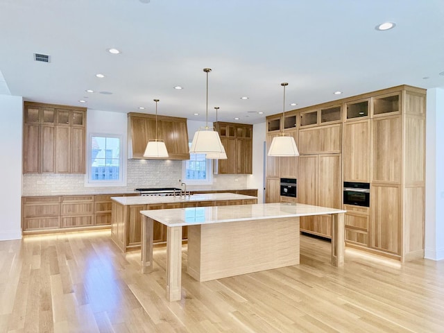 kitchen featuring light wood-style flooring, wall oven, visible vents, black oven, and a spacious island