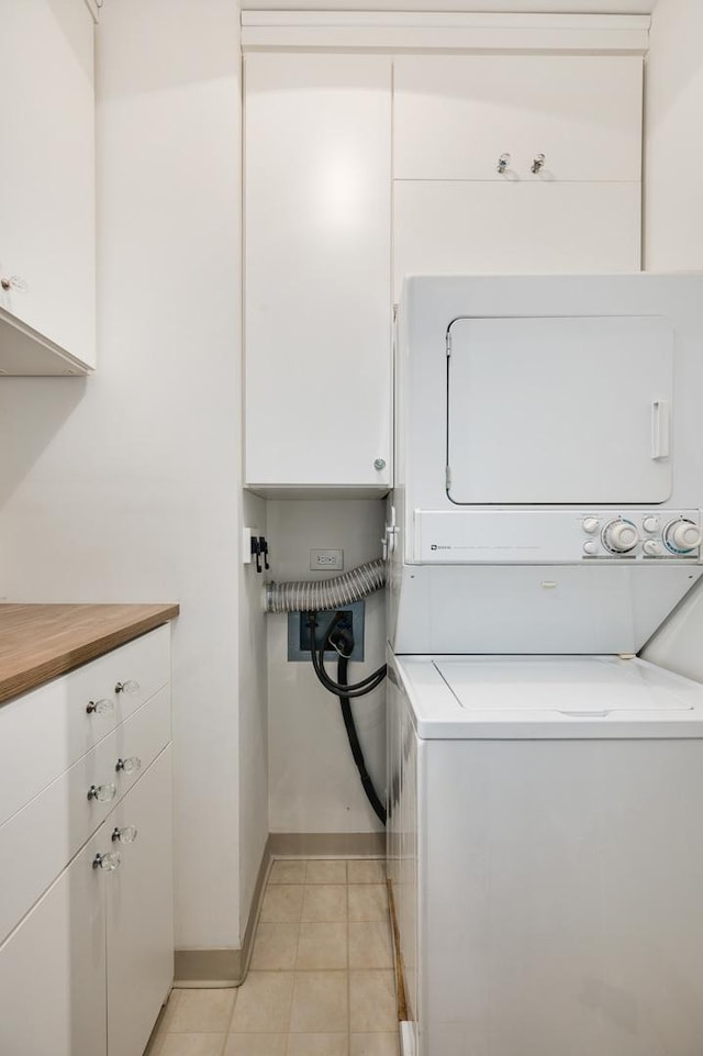 washroom with light tile patterned floors, stacked washer / drying machine, baseboards, and cabinet space