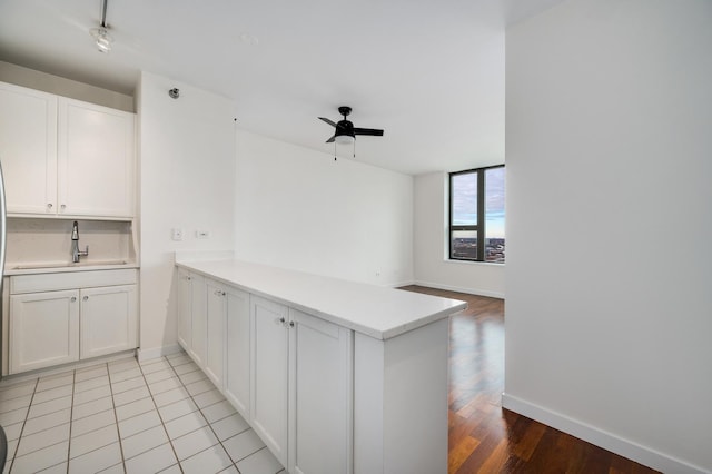kitchen featuring ceiling fan, a peninsula, white cabinetry, light countertops, and a sink