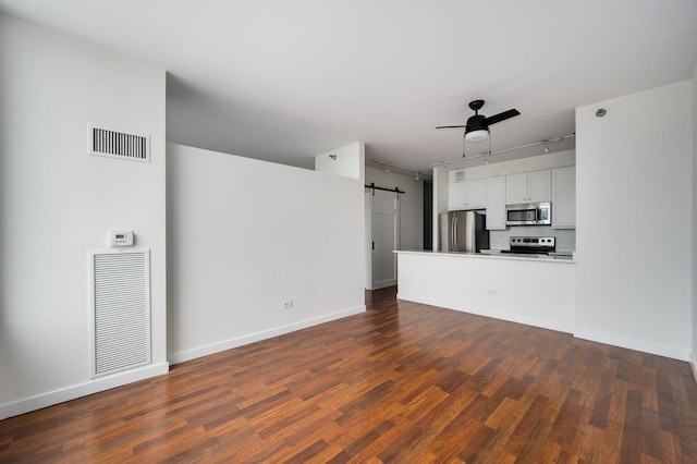 unfurnished living room with dark wood-type flooring, a barn door, visible vents, and ceiling fan