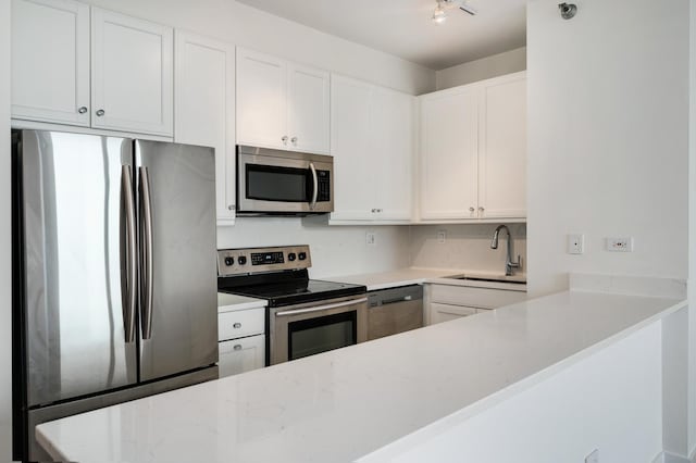 kitchen featuring a sink, appliances with stainless steel finishes, white cabinetry, and light stone countertops