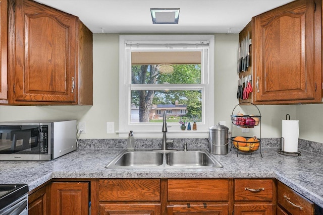 kitchen featuring appliances with stainless steel finishes, a sink, light countertops, and brown cabinetry