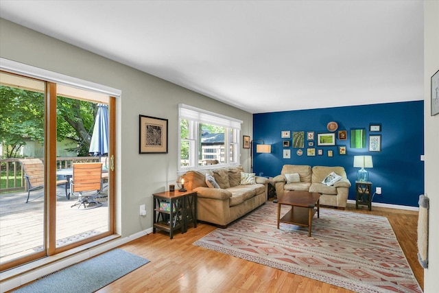 living room featuring wood finished floors, an accent wall, and baseboards