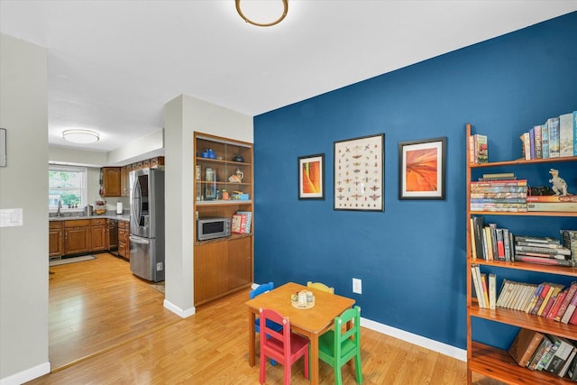 recreation room with light wood-type flooring, a sink, and baseboards