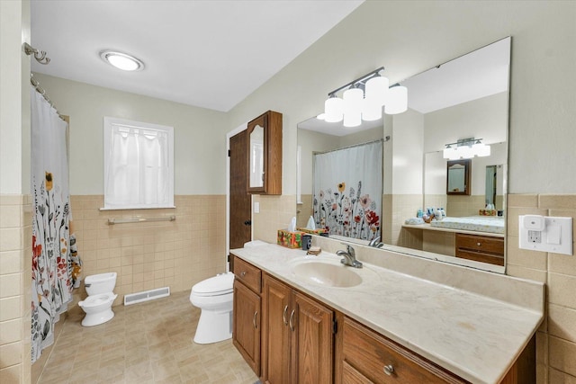 bathroom with tile walls, toilet, a wainscoted wall, and vanity