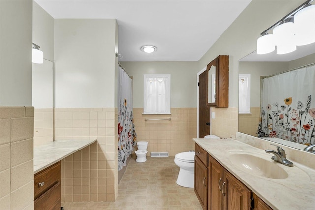 full bath with tile walls, toilet, vanity, a wainscoted wall, and a shower with curtain