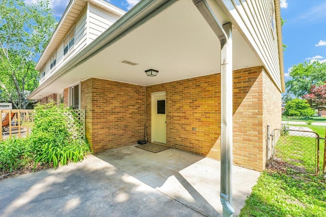 doorway to property featuring brick siding, fence, and a patio