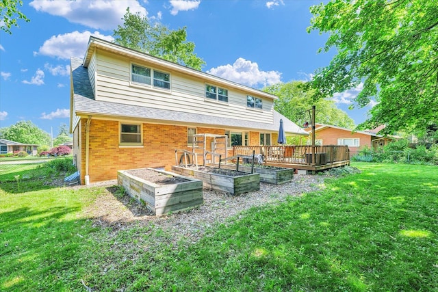 back of property featuring brick siding, a lawn, a vegetable garden, a wooden deck, and roof with shingles
